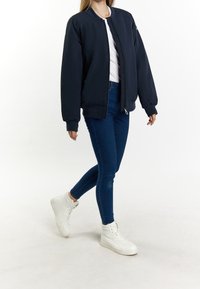 Giubbotto bomber navy con zip frontale, progettato con polsini e orlo a coste. Abbinato a jeans skinny blu scuro e scarpe alte bianche.