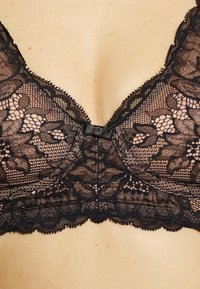 Svart spets-bandeau med blommönster, v-ringad design, vågiga kanter och en central rosett, med en mjuk, strukturerad yta.
