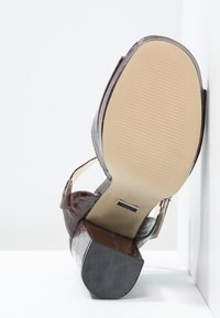 Brown, textured synthetic high-heeled shoe with a slingback strap. Features a rounded toe and a patterned sole for grip.