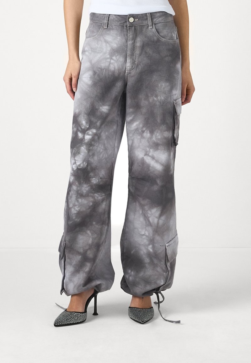 Pantalon cargo large tie-dye gris et noir avec cordons aux chevilles, porté avec des talons pointus noirs ornés de strass.