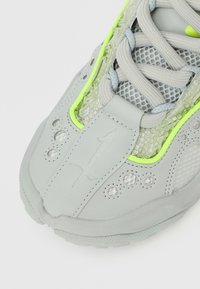 Γκρι αθλητικό παπούτσι με σχεδιασμό από δίχτυ,  νέον πράσινες λεπτομέρειες, λαστιχένια σόλα, υλικά με υφή και εμφανές λογότυπο στο πάνω μέρος.