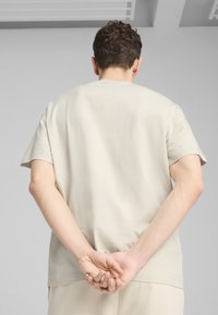 Lys beige bomulds-T-shirt med afslappet pasform, korte ærmer og rund hals, set bagfra. Minimalistisk design, ingen synlige logoer.