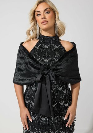 Femme portant une robe noire à sequins style halter avec un châle en fausse fourrure noire noué devant et de longues boucles d'oreilles pendantes en cristal.