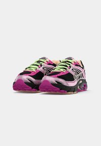 Tênis atléticos com um cabedal em malha preta, detalhes em rosa, verde e roxo, sola texturizada e uma marca proeminente na língua.