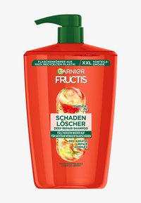 Bouteille en plastique rouge avec un bouchon pompe vert. L'étiquette présente des graphismes colorés et un texte mettant en avant "Shampooing Réparateur Profond" et des ingrédients tels que l'huile de marula.