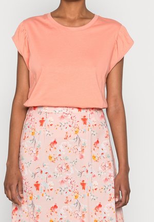 Perzikkleurig T-shirt met korte mouwen en gerimpelde schouders, gecombineerd met een roze rok met bloemmotief met rode, oranje en blauwe bloemen. Soepele stof textuur.