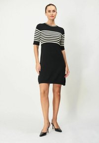 Mustassa neulotussa mekossa on valkoisia vaakasuoria raitoja, lyhyet hihat, pyöreä kaula-aukko ja sivuhalkiot; yhdistetty mustiin kärkitossuihin.