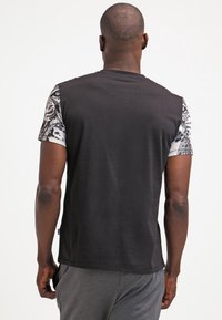 Svart T-shirt med mönstrade kortärmar som har intrikata design. Mjuk tyg med en avslappnad passform och rundad hals.