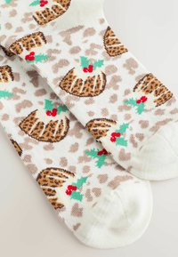 Ceļgalu garuma zeķes ar baltu pamatu, kurām ir brūns leopardu raksts, svētku pudiņi, sarkani ogas un zaļas lapas visā dizainā.