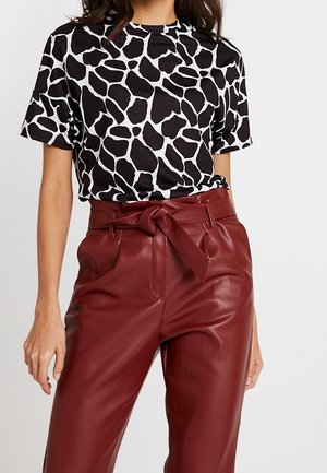 Haut noir à manches courtes avec imprimé girafe blanc, associé à un pantalon en similicuir bordeaux taille haute avec un détail de ceinture nouée.