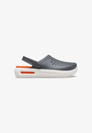 Zueco gris oscuro con orificios de ventilación, suela blanca gruesa con acento naranja y correa ajustable negra en el talón.