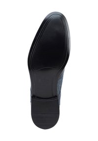 Suela de zapato de goma negra con un patrón de agarre texturizado. Presenta bordes redondeados y una transición suave hacia una parte superior de textil tejido en azul oscuro.