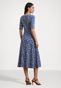 Blå blommönstrad klänning med korta ärmar, figurnära liv och kjol som är utsvängd. Slät tyg och knälång design. Stövlar med remmar.