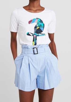 Weißes T-Shirt mit einem bunten Tukangrafik, kombiniert mit hellblauen hochgeschnittenen Shorts mit einem Gürteltaille und vorderen Falten.