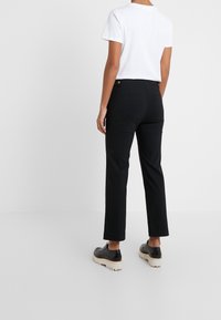 Czarne spodnie o prostym kroju, gładki materiał i dwie tylne kieszenie. Połączone z białą koszulką z krótkim rękawem i czarnymi butami.