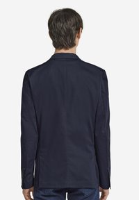 Marinblå blazer med en slät yta, enkel vent, och treknappars detaljer på ärmarna. Rak skärning och klassisk kragsdesign.