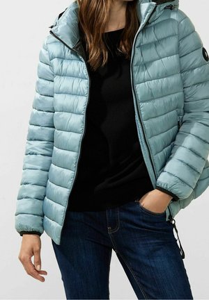 Doudoune bleu clair avec un motif matelassé horizontal, fermeture éclair et capuche. Portée par-dessus un haut noir et un jean en denim. Matériau texturé.