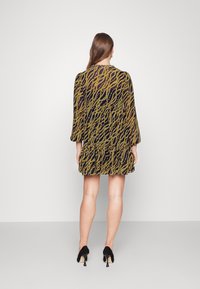 Musta mekko, jossa on keltainen aallonmuotoinen kuvio, pitkät hihat, kerätty vyötärö ja röyhelöhelma. Yhdistetty mustiin korkokenkiin.