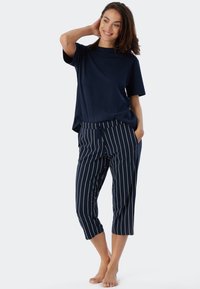 Marinblå kortärmad topp kombinerad med marinblå randiga cropped-byxor. Byxorna har vita vertikala ränder och sidofickor, med en avslappnad passform.