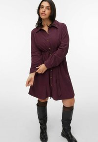 Bordeaux corduroy jurk met een kraag, knoopsluiting en tailleband. Gestyled met kniehoge zwarte laarzen en bruine beenwarmers.