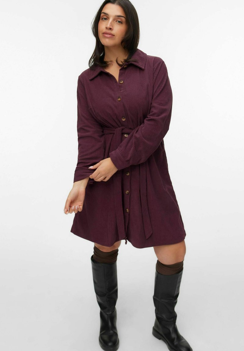 Bordeaux corduroy jurk met een kraag, knoopsluiting en tailleband. Gestyled met kniehoge zwarte laarzen en bruine beenwarmers.