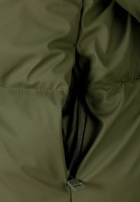 Interno di un giubbotto imbottito verde oliva con una tasca con zip, rivestita in rete nera e dettagli di cucitura a contrasto.