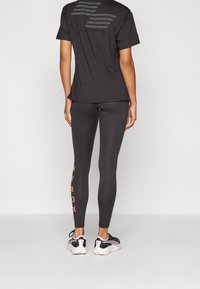 Svart kortärmad skjorta med perforerad rygg, matchad med svarta leggings som har flerfärgade texten "HYROX" på underbenet. Atleterskor.