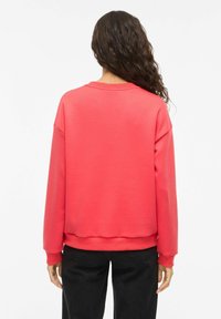 Sweat-shirt rouge avec un col rond et des épaules tombantes. Tissu doux avec poignets et ourlet côtelés, associé à un pantalon noir ample.