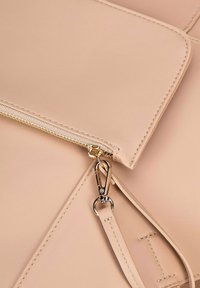 Beige leren handtas met een gouden rits en hardware, met een gladde textuur en een afneembare schouderband. Strakke lijnen en minimalistisch design.