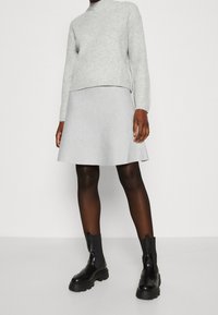 Lichtgrijze geribbelde breisweater met een hoge nek, gecombineerd met een lichtgrijze uitlopende rok, aangevuld met zwarte chunky enkellaarsjes.