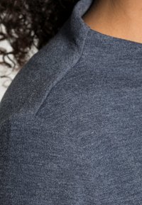 Harmaa t-paita, jossa on pehmeä rakenne, korkea kaulus ja raglan-hihat. Lähikuva korostaa kankaan laatua ja ompelutarkkuutta.
