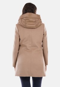 Cappotto beige con finitura testurizzata, caratterizzato da una sezione imbottita sul cappuccio. Maniche lunghe e una vestibilità sagomata. Vista posteriore senza dettagli aggiuntivi.