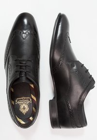 Chaussures habillées en cuir noir avec bout droit orné de perforations décoratives, fermeture à lacets et semelle extérieure texturée. Intérieur avec une semelle intérieure à motif.