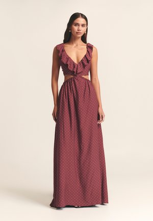 Maxi dress in burgundy fabric with white polka dots, featuring a ruffled V-neckline and cut-out waist, gathered skirt, smooth texture.