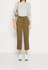Top gris à manches longues, pantalon court olive avec taille à nouer et baskets blanches. Tissu lisse, coupe décontractée et design à longueur de cheville.