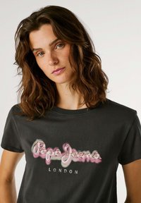 T-shirt preta de algodão com um logo colorido "Pepe Jeans", textura suave, gola redonda e mangas curtas.