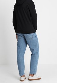 Sudadera con capucha negra, jeans anchos de color azul claro y zapatillas blancas con suelas marrones; la vista desde atrás resalta el estilo y el ajuste casual.