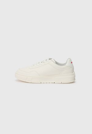 Białe niskie sneakersy ze sznurowadłami, amortyzowaną podeszwą i delikatnymi przeszyciami, pokazane z boku na jednolitym jasnym tle.