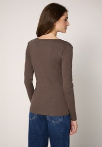 Braunes Langarmshirt mit Rundhalsausschnitt aus Rippstoff, kombiniert mit blauen Jeans mit Gesäßtaschen.