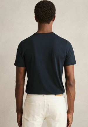 Tricou negru din bumbac cu mâneci scurte și guler rotund, asociat cu pantaloni albi. Textură netedă, design minimalist, fără modele vizibile.