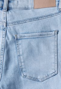 Jasnoniebieska tkanina dżinsowa z pojedynczą tylną kieszenią i prostokątną skórzaną łatą powyżej. Szwy są widoczne i starannie wykończone.