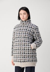 Strick-Pufferjacke mit hohem Kragen, präsentiert ein braun-schwarzes Schachbrettmuster auf cremigem Hintergrund, mit gerippten Bündchen und Saum.