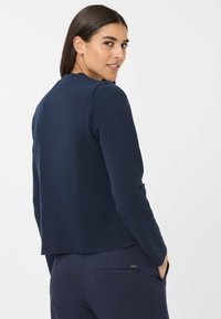 Dunkelblaue Strickjacke mit langen Ärmeln, rundem Ausschnitt und subtiler Textur. Verfügt über einen verkürzten hinteren Saum und ein elegantes Design.