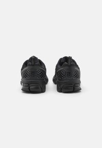 Des chaussures de sport noires avec un dessus en maille, des accents texturés et une semelle en caoutchouc épaisse. Elles possèdent une languette et des motifs géométriques sur les côtés.
