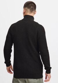 Schwarzer, gerippter Strickpullover mit hohem Kragen, langen Ärmeln und lockerer Passform, der eine strukturierte Oberfläche und auffällige Bündchen an den Handgelenken aufweist.
