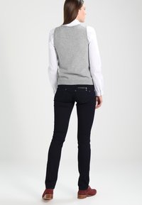 Chaleco de punto gris sobre una camisa blanca con cuello, combinado con jeans skinny oscuros. El atuendo incluye botas de tobillo de ante rojas.
