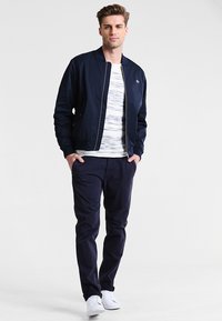 Veste de pilote navy, à fermeture éclair sur le devant, avec des poignets côtelés, associée à un t-shirt rayé et un pantalon navy, complétée par des baskets blanches.