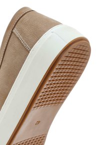 Zapatilla de ante beige con un upper texturizado, entresuela blanca contrastante y una suela de goma marrón con un agarre patrón.