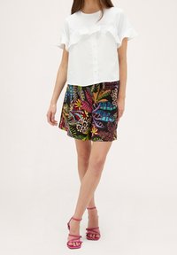 Blouse blanche à manches courtes avec des volants, associée à un short noir à motif de feuilles tropicales colorées. Accessoirisée avec des sandales roses à brides.