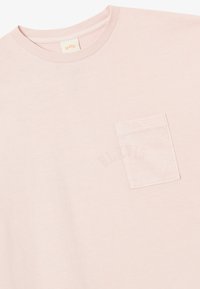Tricou din bumbac roz deschis, cu guler rotund, mâneci scurte și un buzunar pe pieptul stâng, având un logo discret al mărcii.